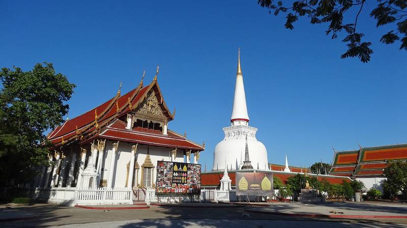 พระบรมธาตุเจดีย์ทรงระฆังสีขาวสูงเด่นหลังพระวิหารหลังคาสีส้ม